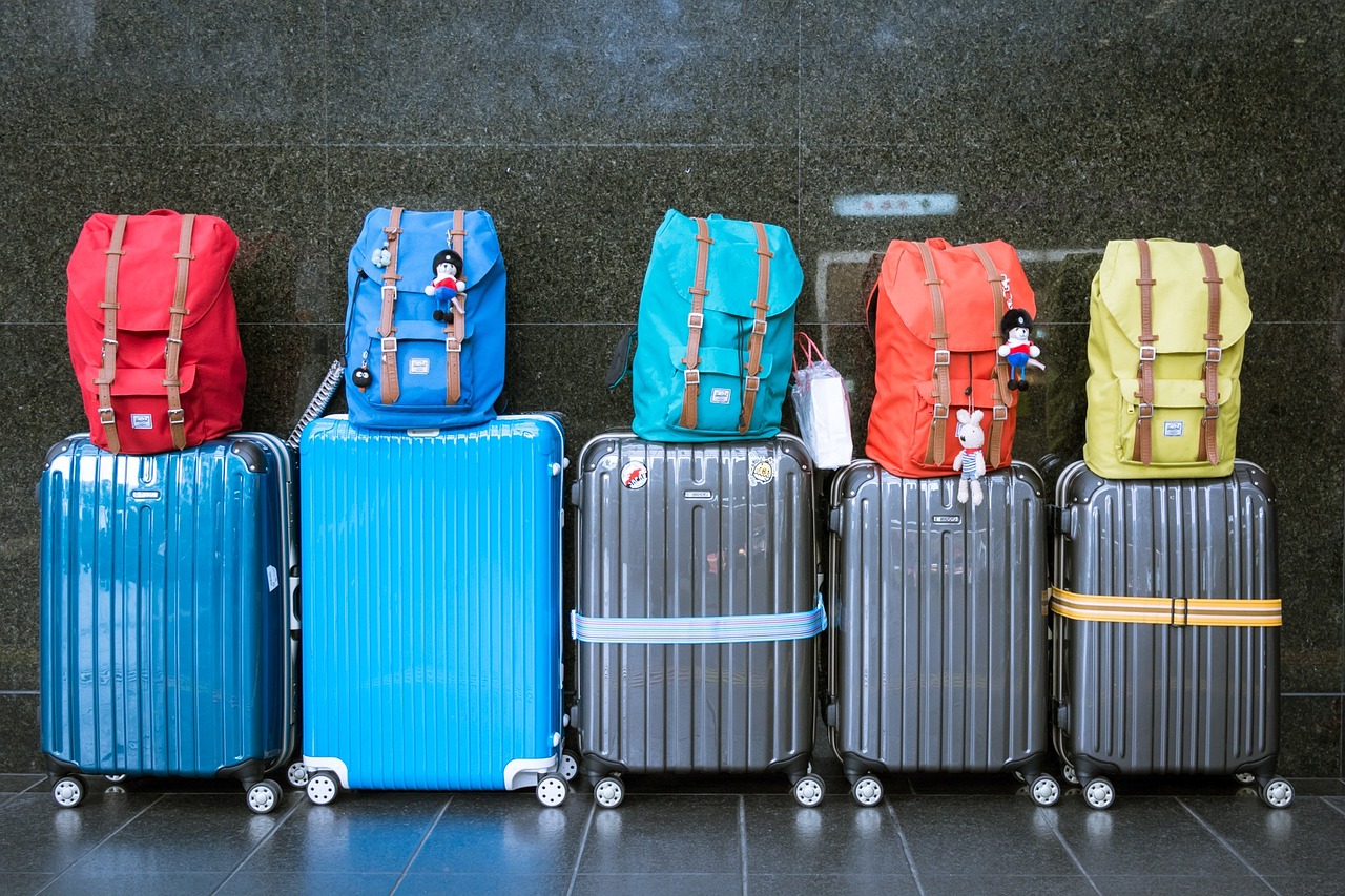 Five beat up suitcases with backpacks on top in front of a marble wall