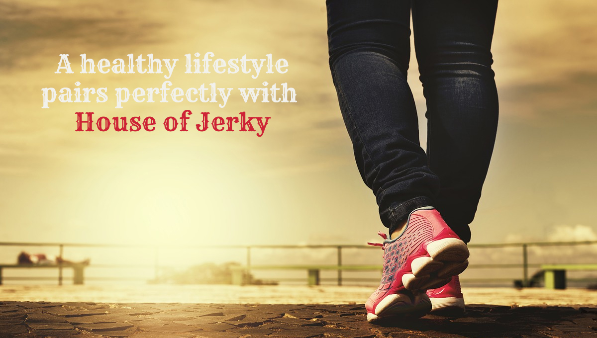 The words A healthy lifestyle pairs perfectly with House of Jerky on the left hand side with a pair of legs wearing jeans and pink shoes on the right an a background of a metal railing an sky background